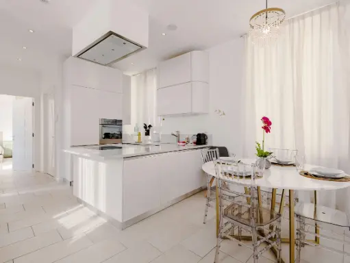 Cocina moderna y luminosa con diseño minimalista en tonos blancos, con una pequeña mesa de comedor y sillas transparentes.