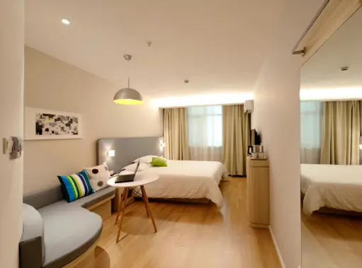 Habitación moderna y luminosa con suelo de madera clara, una cama doble grande y un sofá pequeño en la esquina con cojines coloridos..